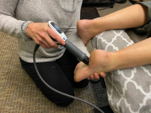 A chiropractor applies shockwave therapy to a patient's heel to treat plantar fasciitis.