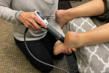 A chiropractor applies shockwave therapy to a patient's heel to treat plantar fasciitis.