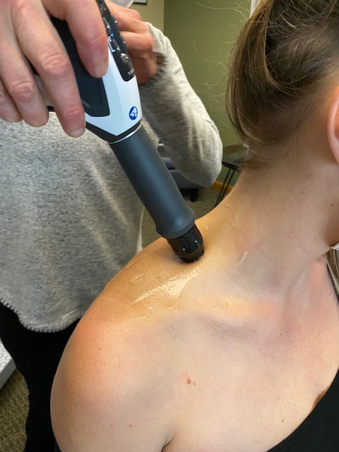 Close up view of a chiropractor applying shockwave therapy to a patient's neck and shoulder to heal musculoskeletal issue. 