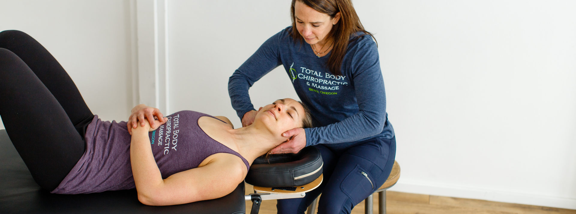 A chiropractor sitting working on the neck of a patient.