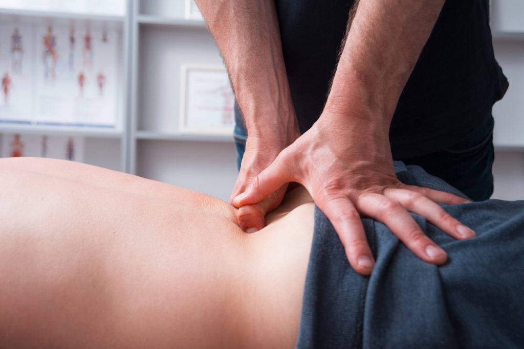 A male massage therapist performing deep tissue massage on the lower back of a male patient.