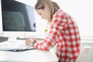 Woman with bad posture sitting hunched over at her desk in front of a computer typing on a keyboard.