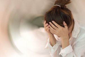 Woman holding her head with a blurred background to depict she is suffering from dizziness and vertigo.