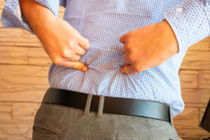 A close up view of the backside of a man in a dress shirt pointing his fingers where he is having lower back pain.