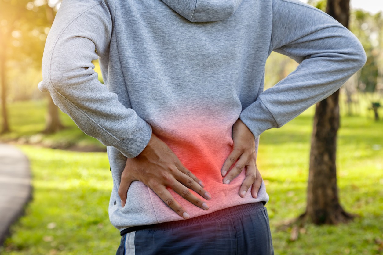 A close up view of an African American female runner in a gray hoodie holding her lower back due to back pain.