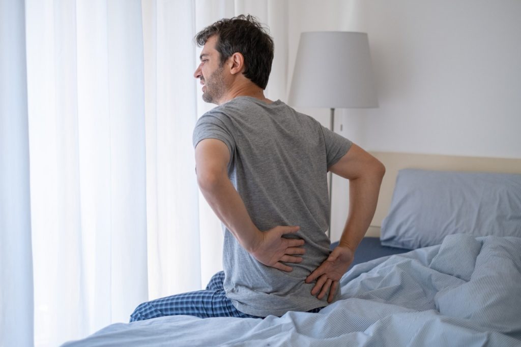A man sitting on his bed after waking up with lower back pain.