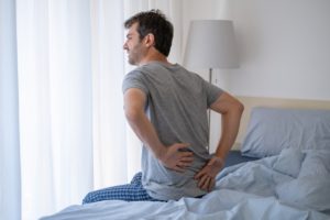 Man sitting on bed with lower back pain.