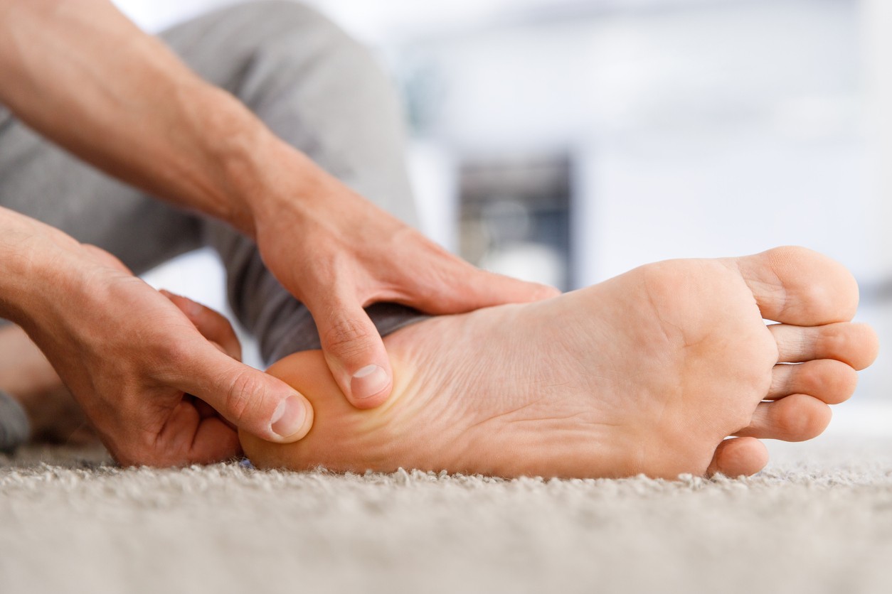 Close up of a man rubbing and holding his heel from plantar fasciitis pain.