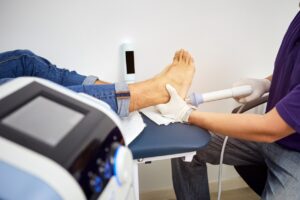 A chiropractor using shockwave therapy on a man's heel for plantar fasciitis.
