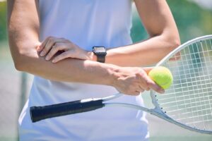Close up view of a female tennis player holding her racquet in one hand and her elbow with the other due to tennis elbow pain.