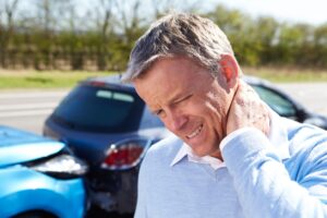 Man rubbing neck pain after a car accident with two crashed vehicles in the background.