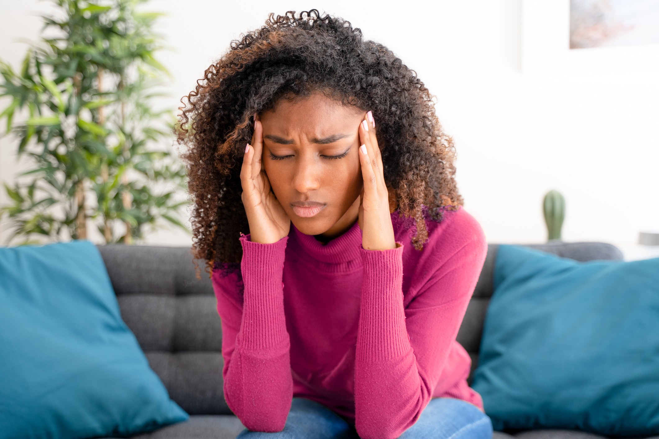 A black woman sits on the sofa and holds her head from tension headache pain.