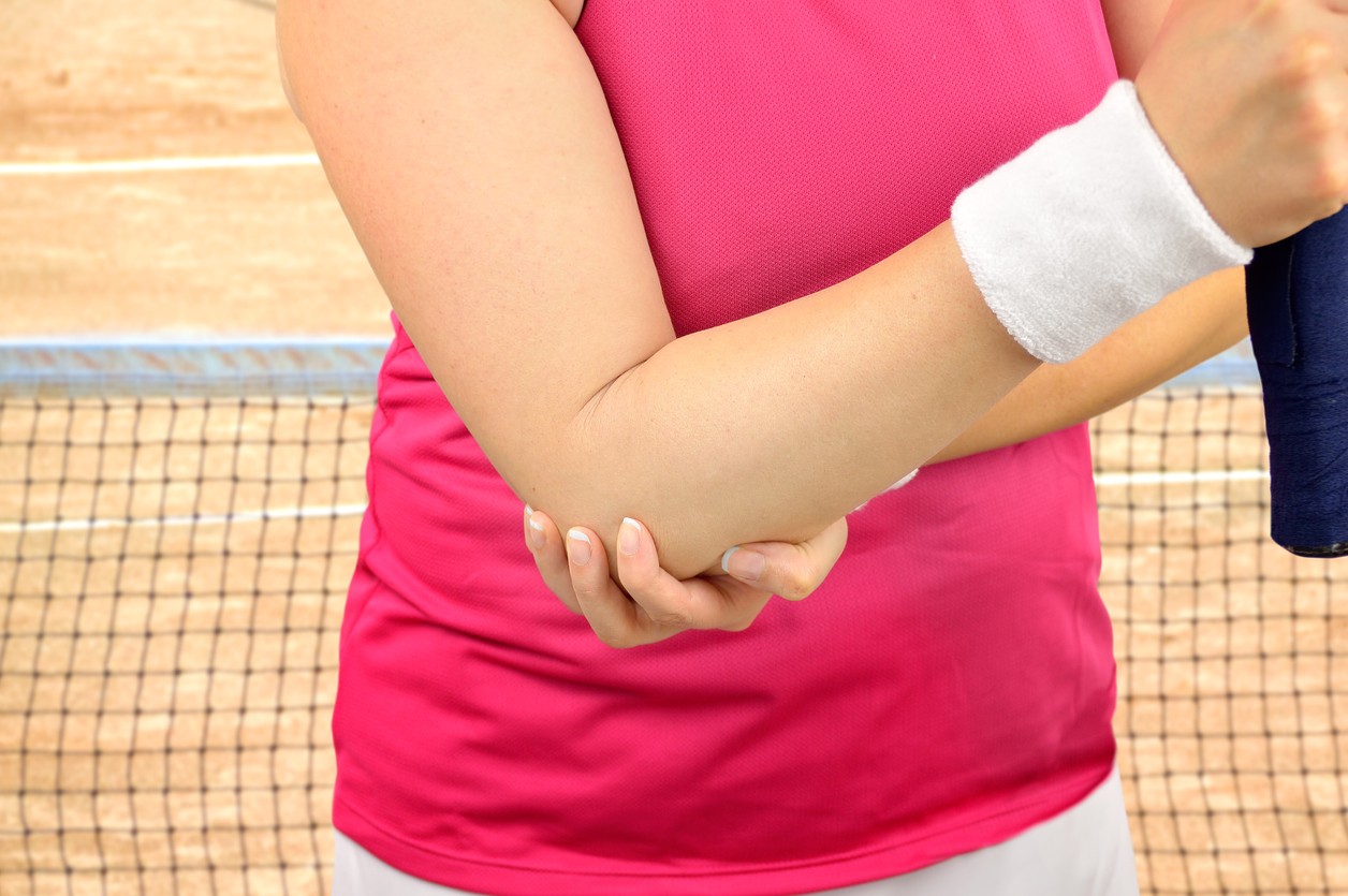 A woman tennis player holds her elbow from tendonitis pain while on the tennis court. 