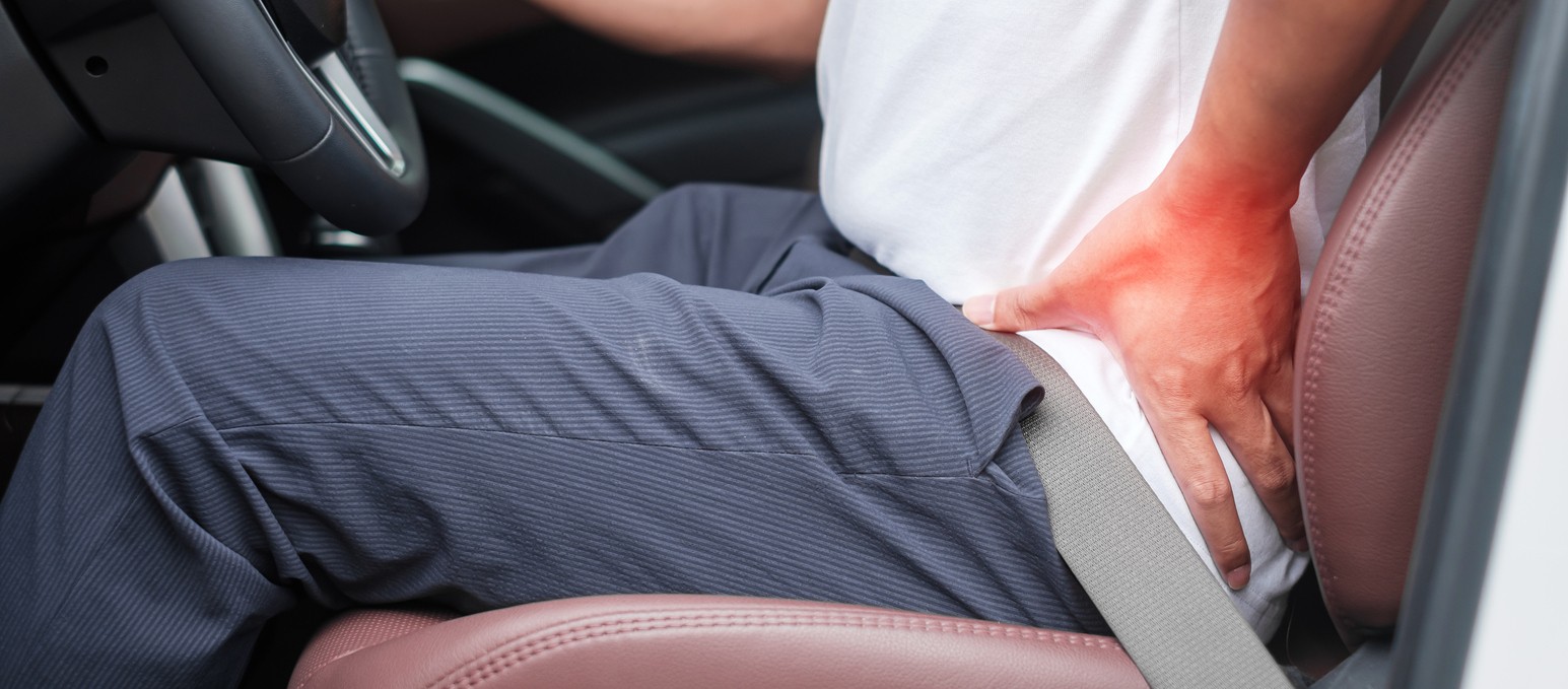 Man sitting in car holds his lower back from piriformis syndrome pain.