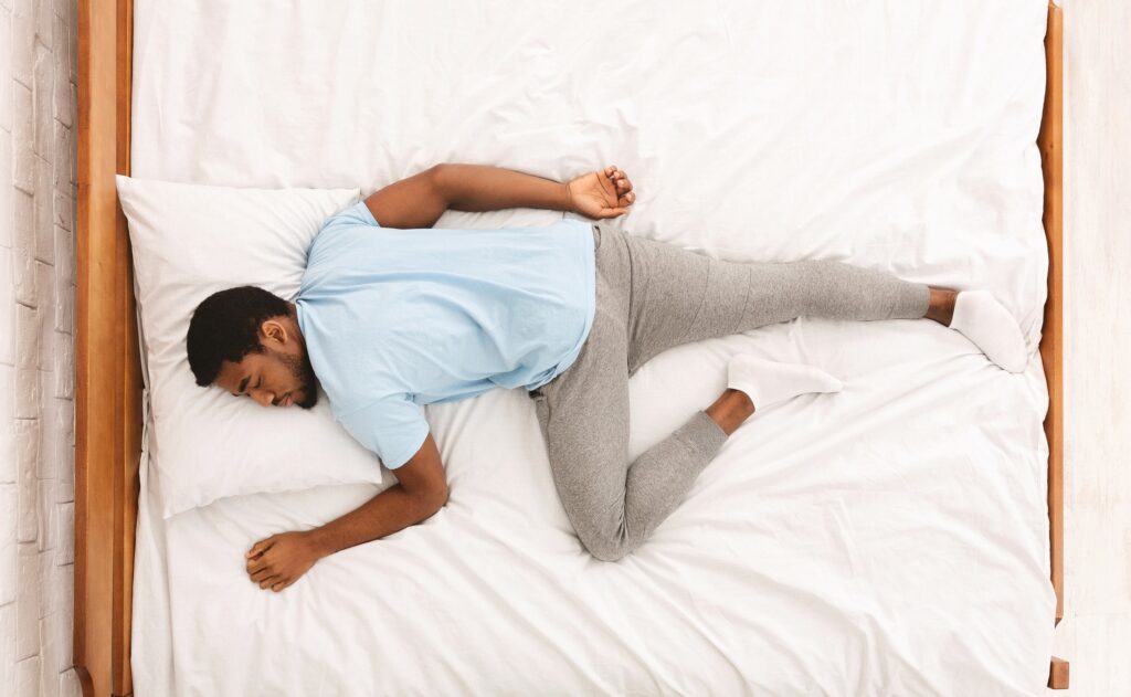 An African-American man sleeps on his stomach in bed, causing neck pain. 