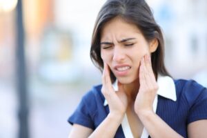 A woman holds her jaw with TMJ pain which can be treated with chiropractic care.