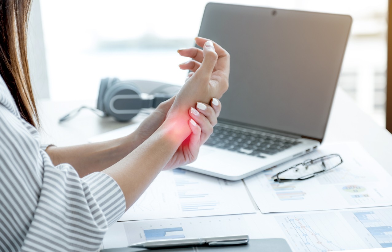 A woman sitting in front of a laptop holding her wrist in pain from tendonitis.