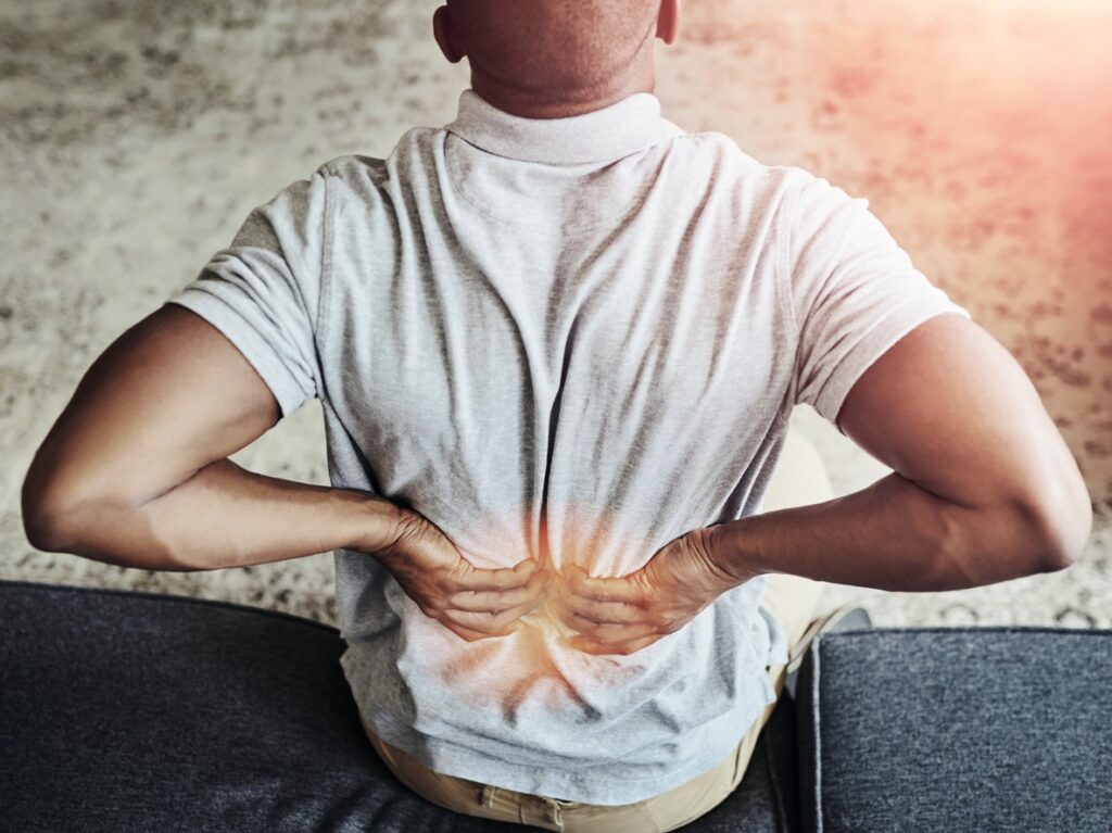 Close up view from behind of an African-American man holding his lower back in pain from a herniated disc.