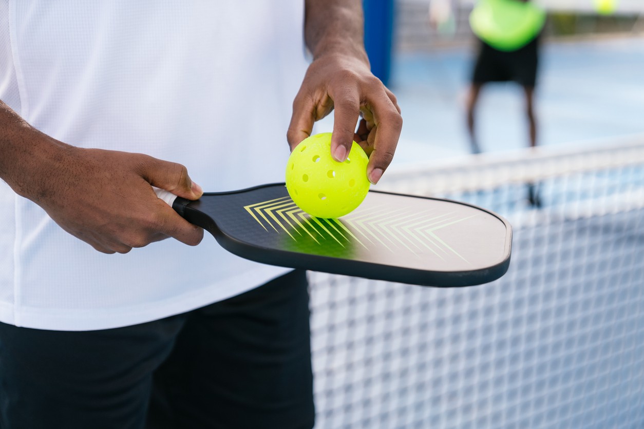 Close up of a man holding a paddle and pickleball. 