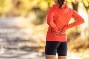 A female runner stands on a trail holding her lower back from sciatica pain.
