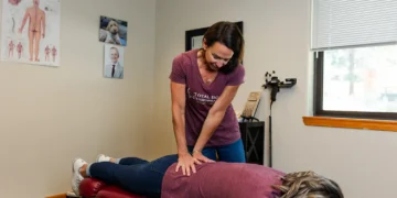 A therapist provides a massage to a client lying on a red treatment table in a clinical setting.