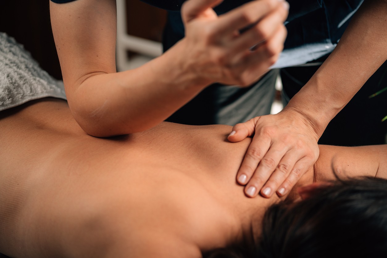 A female massage therapist performs deep tissue massage on the back of a female patient. 