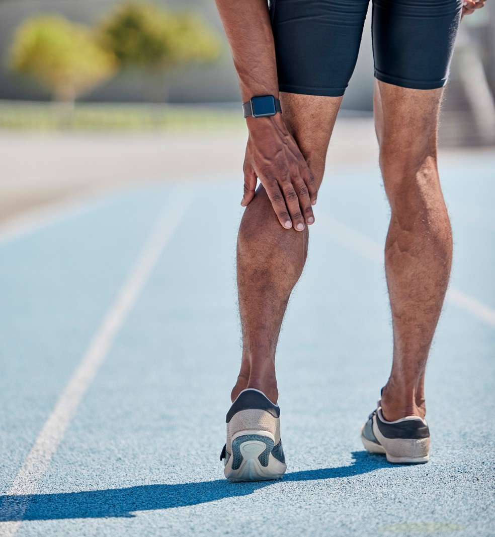 A male runner grabs the back of his calf in pain while training on an outdoor track. 