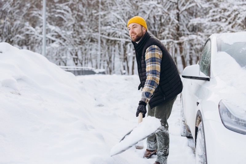 A man shovels heavy snow in a driveway, straining his lower back. 