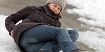 A woman slips and falls on ice and rubs her back in pain.
