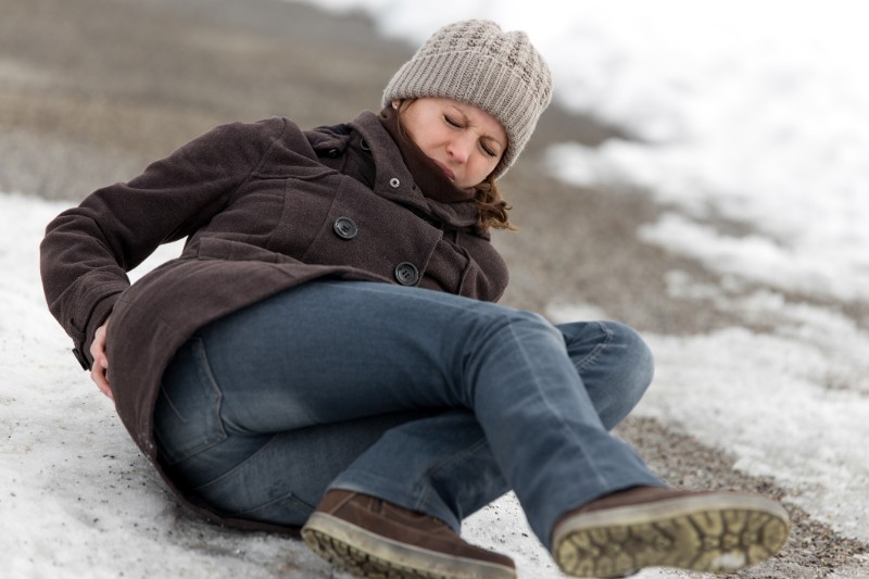 A woman slips and falls on ice and rubs her back in pain.